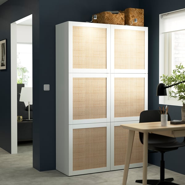 Tall white BESTÅ storage with beige doors against blue wall beside doorway.