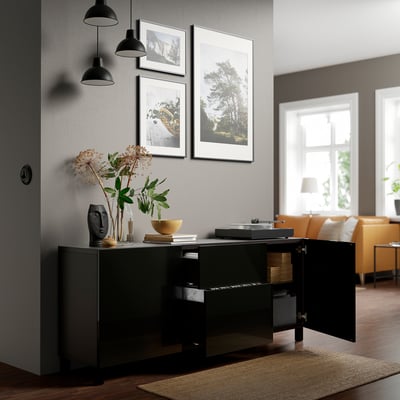 Modern living room with black sideboard displaying decor, artwork, and orange sofas. Two black pendant lamps provide lighting.