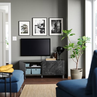 Modern living room with BESTÅ tv bench, flat screen, blue sofa, rug, plant & artwork on grey wall.