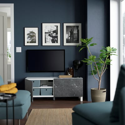 Modern living room with teal chairs, flat-screen tv on stand, and framed photos. Cable management seen through open compartments.
