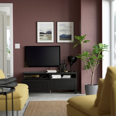 Modern living room with maroon walls, yellow sofa, tv stand, flat screen, mountain photos, and plant.