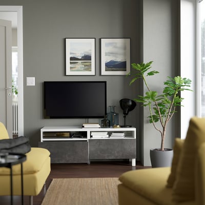 Modern living room with tv on storage console, featuring two framed nature photos, a tall plant, and yellow furniture.
