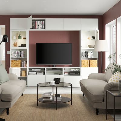 Modern living room with grey sofas, glass coffee table, tv, books, decor, burgundy walls, beige rug.