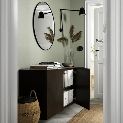 A modern hallway a wall-mounted BESTÅ storage unit with open doors revealing storage boxes. Above it, a round mirror and wall lamps enhance the decor.
