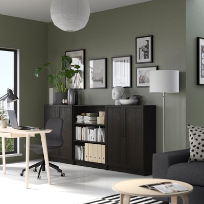 Wooden BILLY bookcase against green wall, filled with books and decor. Next to office chair and desk.