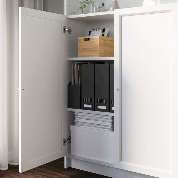 Open white cabinet reveals organised storage. Top shelf has wooden box, middle has black file folders, bottom has stacked papers.