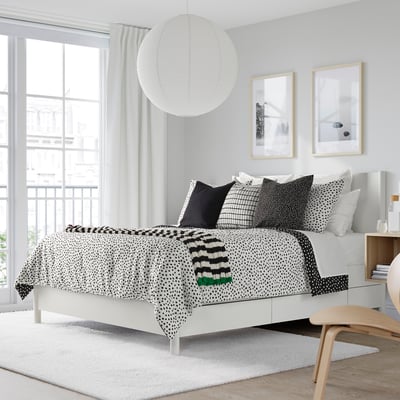 Bedroom with BJÖRKGRÅMAL black & white comforter, minimalist decor, large window, wooden stool.