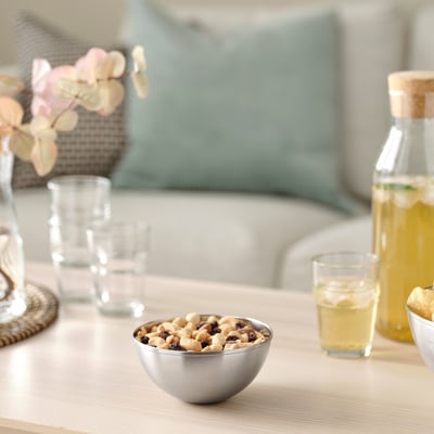 Small stainless steel bowl with mixed nuts on a table with glasses and a jug.