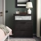 Black BRIMNES chest of drawers with frosted glass top, situated between a bed and a curtain, reflecting a stylish and organised bedroom setup.