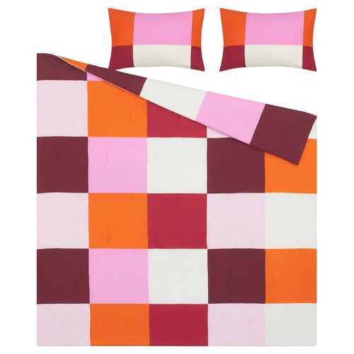 Chequered bedspread with orange, pink, white, and red squares and matching pillows on white background.
