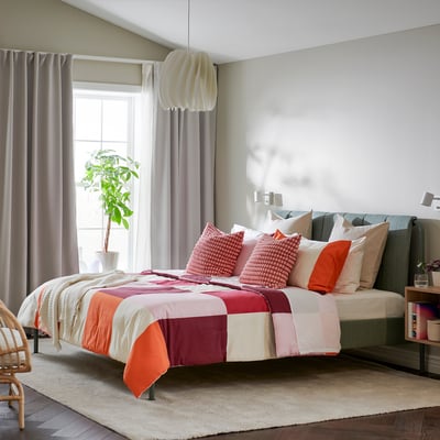 Orange and white chequered BRUNKRISSLA comforter with pillows on bed against wall with light and window.