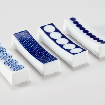 Four white porcelain chopstick holders with blue patterns lie diagonally. Each unique designs, from dots to lines, showcasing detailed craftsmanship.