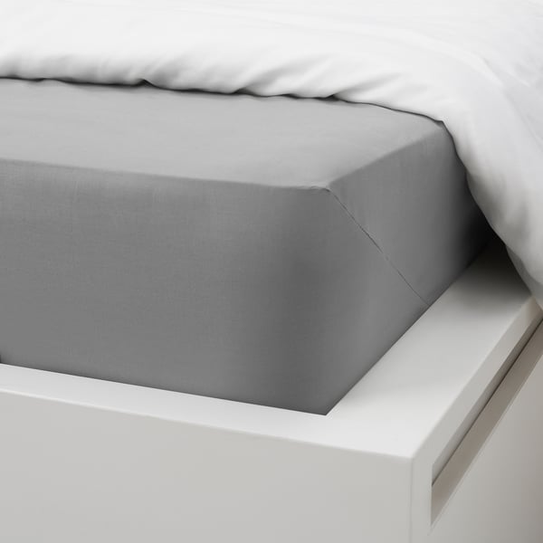 Image shows a neatly made bed with grey cotton sheets. The fitted sheets elastic edge is visible, fitting mattresses up to 26 cm thick.