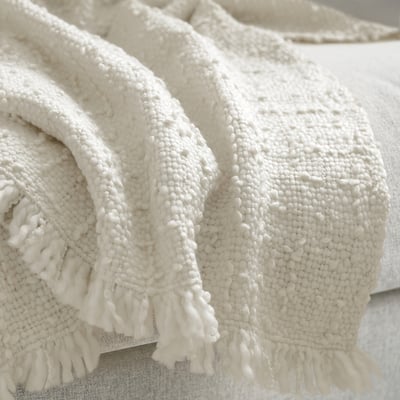 White woven blanket with fringe on edges, folded on bed.