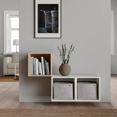 Minimalist wall-mounted shelving unit with grey boxes, a bookcase, and a vase with flowers, decorated in a neutral and modern design.