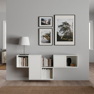 Modern living room with grey wall featuring white storage unit holding books and a lamp, topped with three framed nature photos.