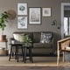 Living room with olive sofa, cushions, rug, side table, plants, gallery wall, and green lamp.