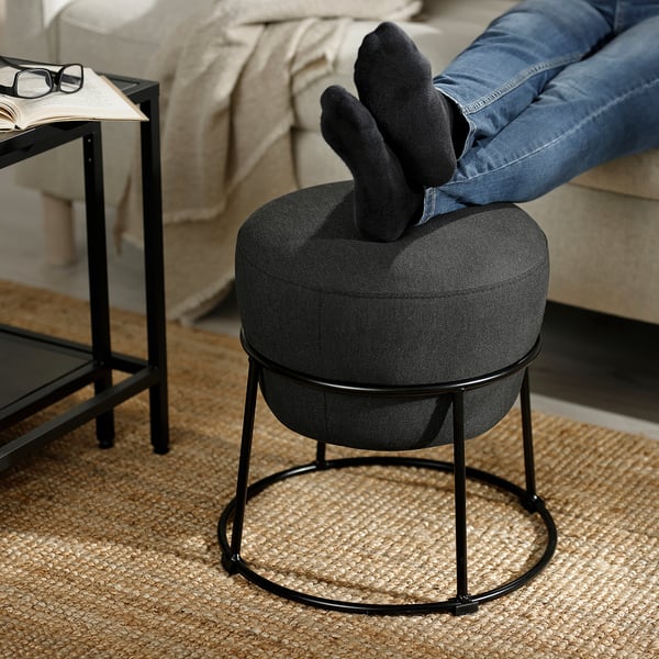 Feet on small grey footstool by side table with book and glass.