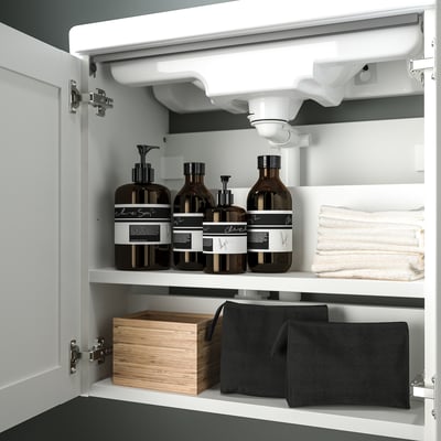 Open bathroom cabinet with shelves. Towels, dark brown bottles with labels, and storage boxes inside. White framed door.