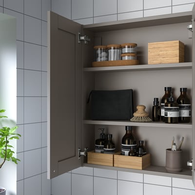 Open grey wall cabinet with shelves, neatly storing bottles, jars, and boxes, part of IKEAs ENHET series for organised kitchen or bathroom storage.