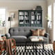 Modern living room featuring ESSEBODA grey sofa, black coffee table, plaid rug, dark wooden bookcase, and two floor lamps.
