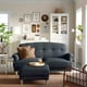 Modern living room with dark blue ESSEBODA sofa and ottoman, brown throw pillow, white cabinet, and plants.