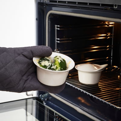 Hand holds dish with broccoli and cheese near oven, ready for baking.