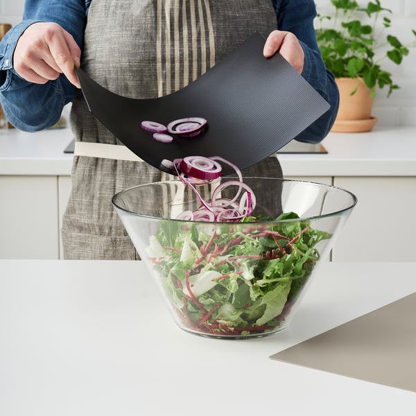 Person slices onions on flexible cutting board, sliding slices into salad bowl. The boards flexibility helps guide the food neatly.