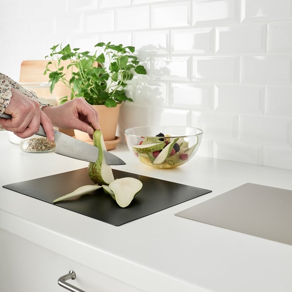 Person slices fruit on flexible cutting board near bowl of fruit and plant.