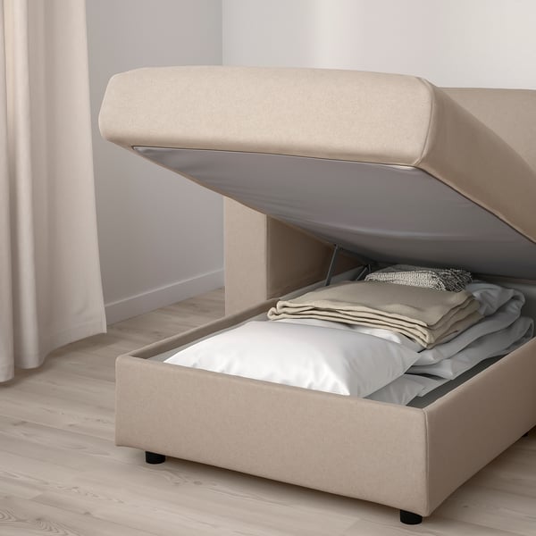 Beige FINNALA sofa-bed with storage. Lid open, showing folded blankets and mattress.
