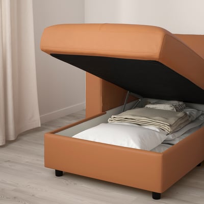 FINNALA sofa-bed with storage open, showing folded blankets inside, set on a light wooden floor.