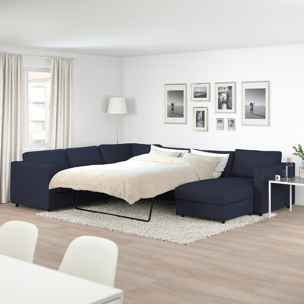 L-shaped navy blue FINNALA sofa-bed with chaise, white decor, black-and-white art, wooden floors.