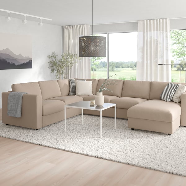 Modern living room with beige FINNALA l-shaped sofa-bed, white coffee table, and large window. Sofas chaise section can be positioned left or right.
