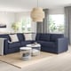 Modern living area with FINNALA navy blue sectional sofa, white pillows, wire coffee table, jute rug, and large windows with curtains.
