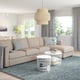 Modern living room with beige sofa and white coffee tables. Large windows with grey curtains and unique light fixture.