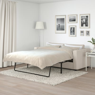 FINNALA beige sofa-bed with clean lines, medium size, framed art, lamps, and curtains. Comfortable for modern living.