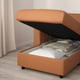 Orange sofa-bed open, revealing storage space with folded bedding.