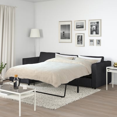 Modern bedroom with FINNALA black sofa-bed, white pillows, black & white photos, white lamp, side tables. Spacious and minimalist.