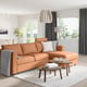 Modern living room with FINNALA sectional sofa in camel leather, wood coffee tables, hanging lamp, large window with view, white curtains.