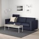 Modern living room with FINNALA dark grey sofa, white coffee table, and wall art. Sofa has 3 seats, 2 pillows, and a headrest.