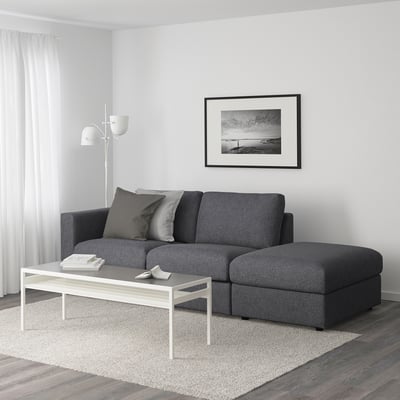 Modern living room with FINNALA grey sectional sofa, coffee table, lamp, coastal photo, and beige rug.