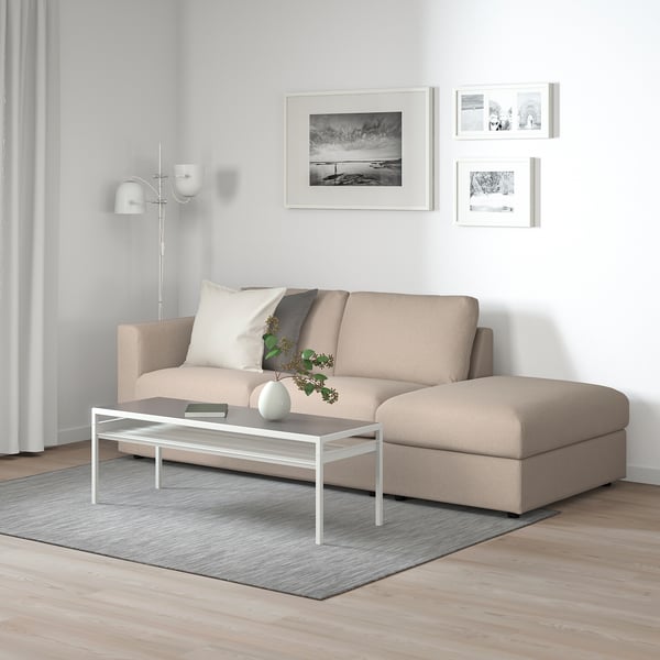 Minimalist living room with FINNALA beige sectional sofa, white coffee table, grey rug, and black & white wall art.