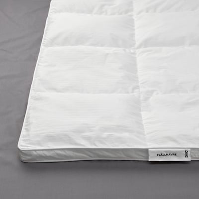 White duvet with stitched sides on a bed, showing soft, thick, and fluffy texture. Brand label FJÄLLHAVRE visible at edge.