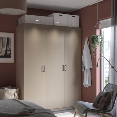 Modern closet with beige doors and white boxes, located near a window with a hanging plant and a chair.