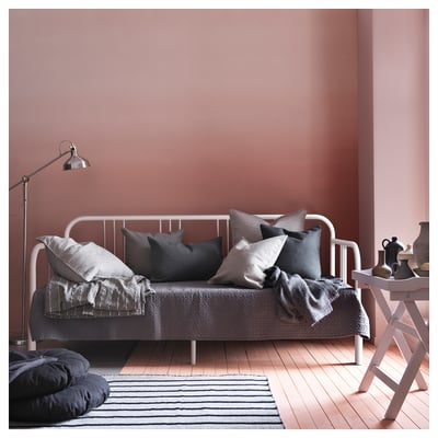 Modern white day-bed with grey bedding, pillows, and rug in cosy room.