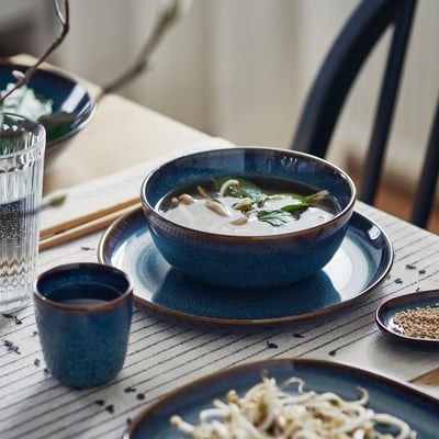 Blue bowl with soup, dish, and cup on table, rustic design.