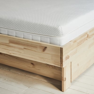 Close-up of well-made mattress on sturdy pine bed frame. Mattress is firm and textured.