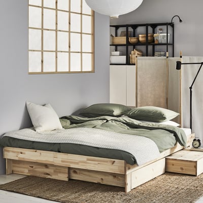 Minimalist bedroom with pine GLAMBERGET extendable bed, green linens, white walls, and large window.