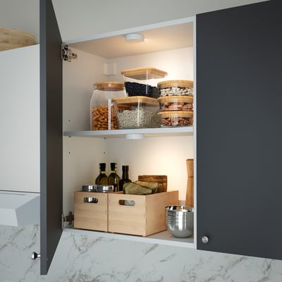 Cabinet with led motion sensor light illuminating organised food containers and storage boxes.