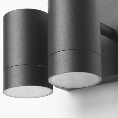 Modern outdoor wall lamp with two cylindrical shades, emitting soft light.